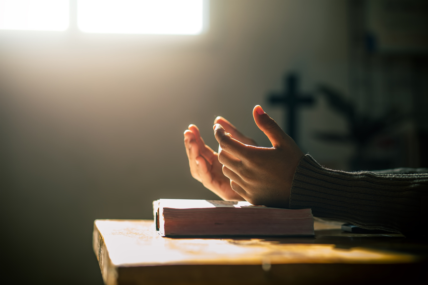 Christian hands praying on holy bible in light of morning at